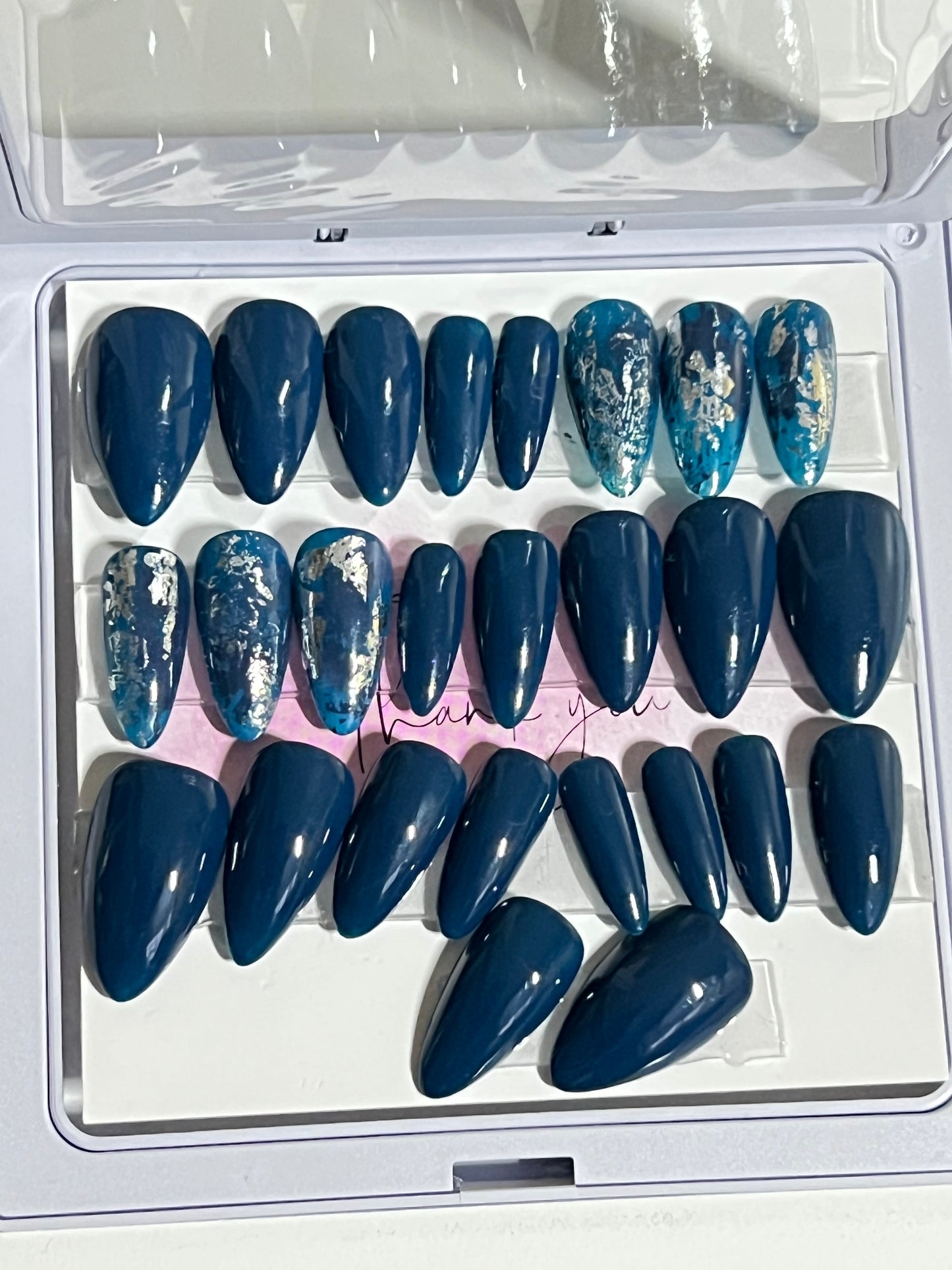 Set of 20 solid dark blue/teal short stiletto nails with 6 accents and darker blue and silver foil. No stain top coat.