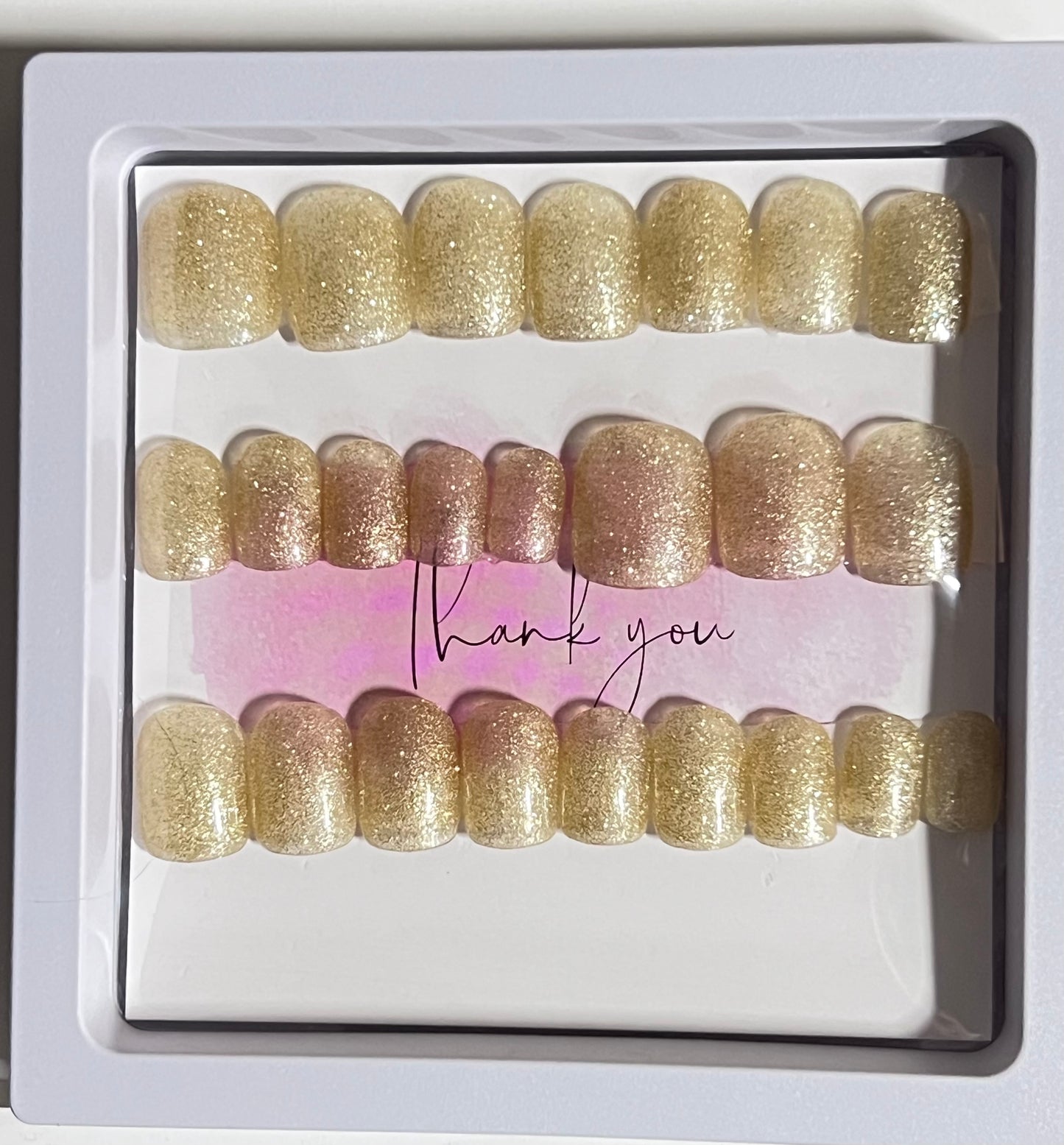 Set of 24 short square nails with gold glitter gel polish and no stain top coat.