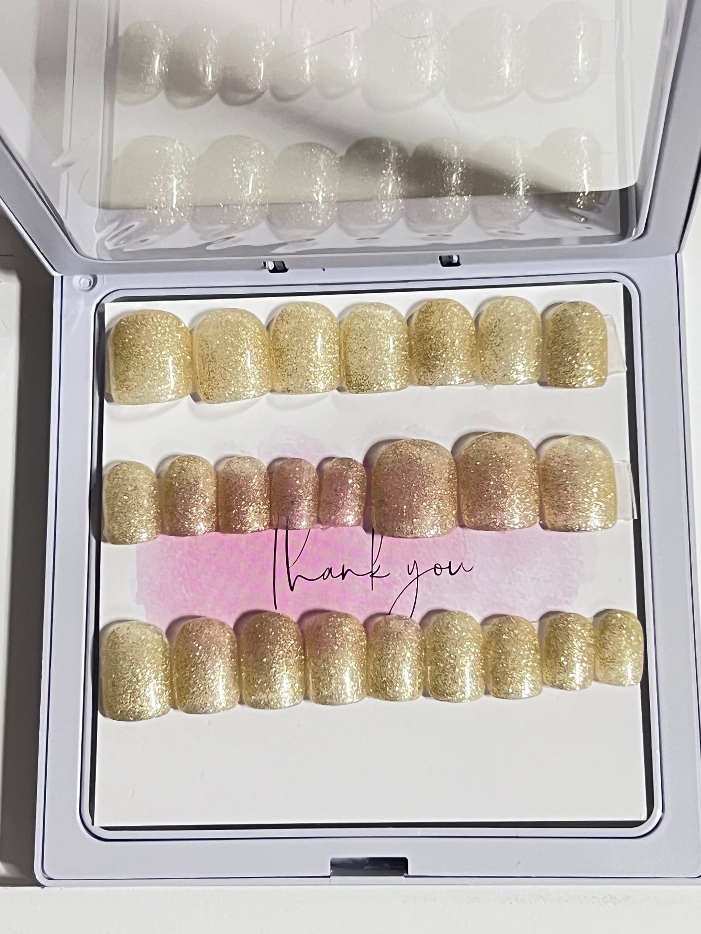 Set of 24 short square nails with gold glitter gel polish and no stain top coat.