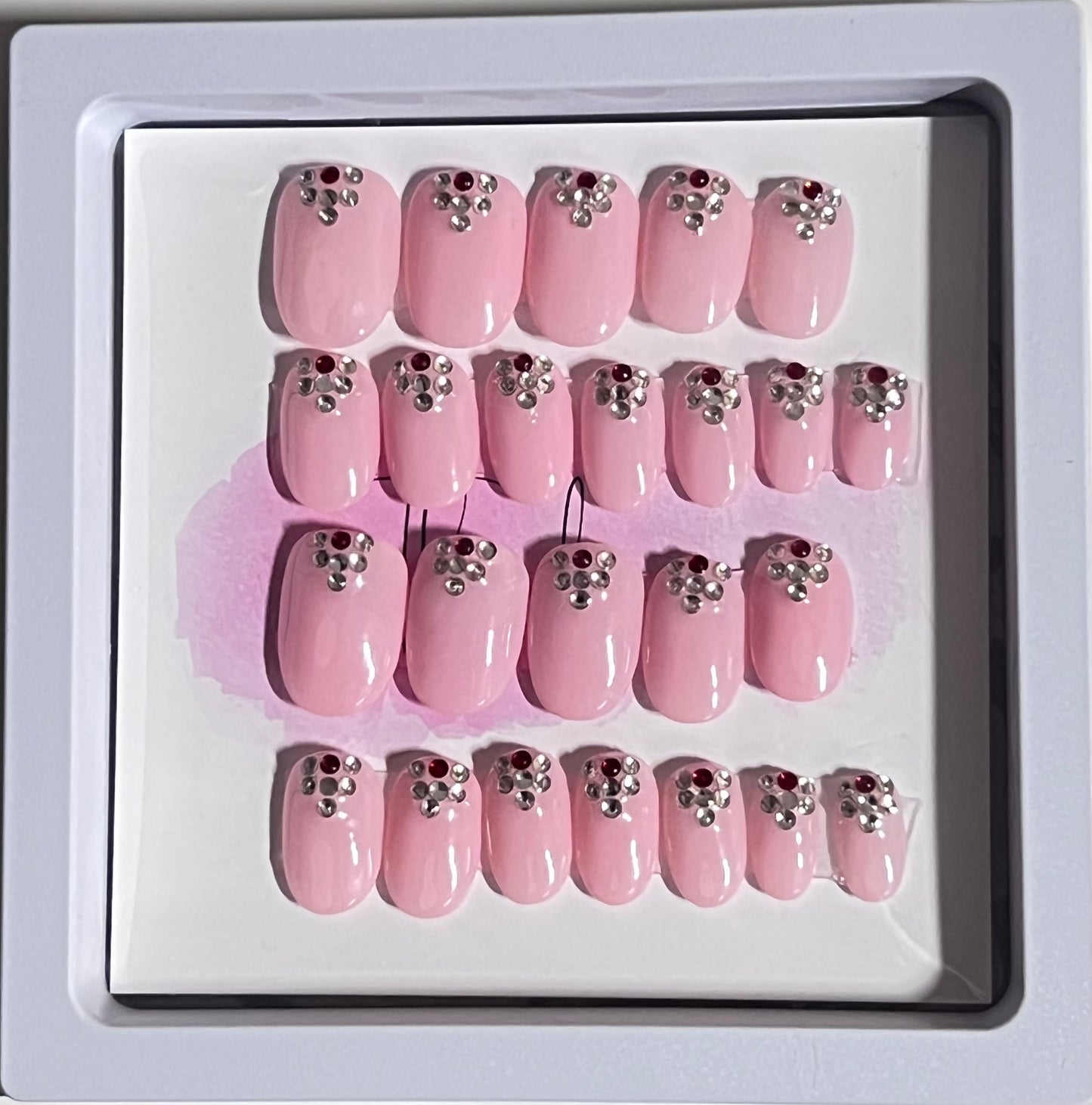 Set of 24 extra short oval nails with a light pink gel polish and stones at the cuticle sealed with a hard gel top coat.