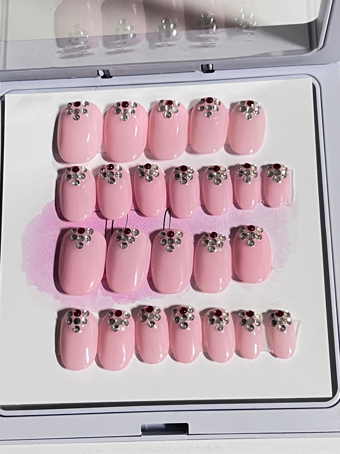 Set of 24 extra short oval nails with a light pink gel polish and stones at the cuticle sealed with a hard gel top coat.
