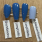 Four false nail tips in shades of blue and pale blue, labeled ShortAlmond, LongCoffin, LongStiletto, and M MediumSquare, displayed on a wooden surface.
