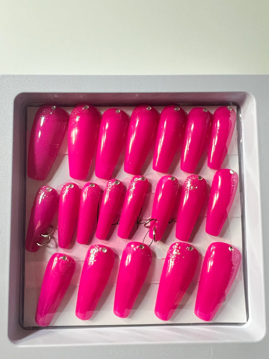 Set of 20 long coffin press-on nails with pink gel polish. Rhinestones at  the cuticle and slight silver glitter (faintly) and two pierced nails with O rings & sealed with hard gel.