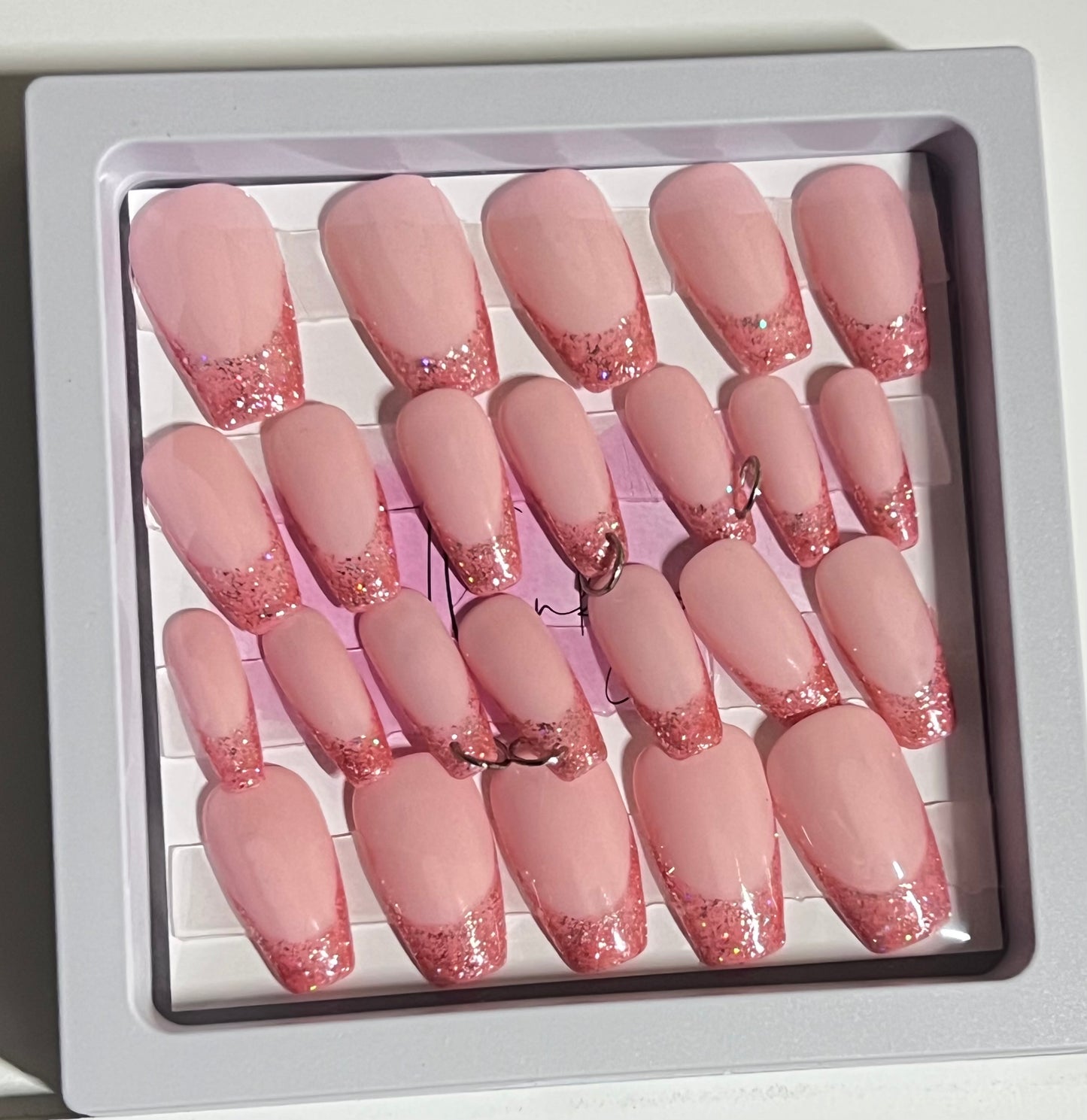 Set of 24 medium length coffin shaped nails with light pink/peach base and darker pink with glitter french tip. Included are 4 nails that are pierced with silver O rings and all are sealed with hard gel top coat.