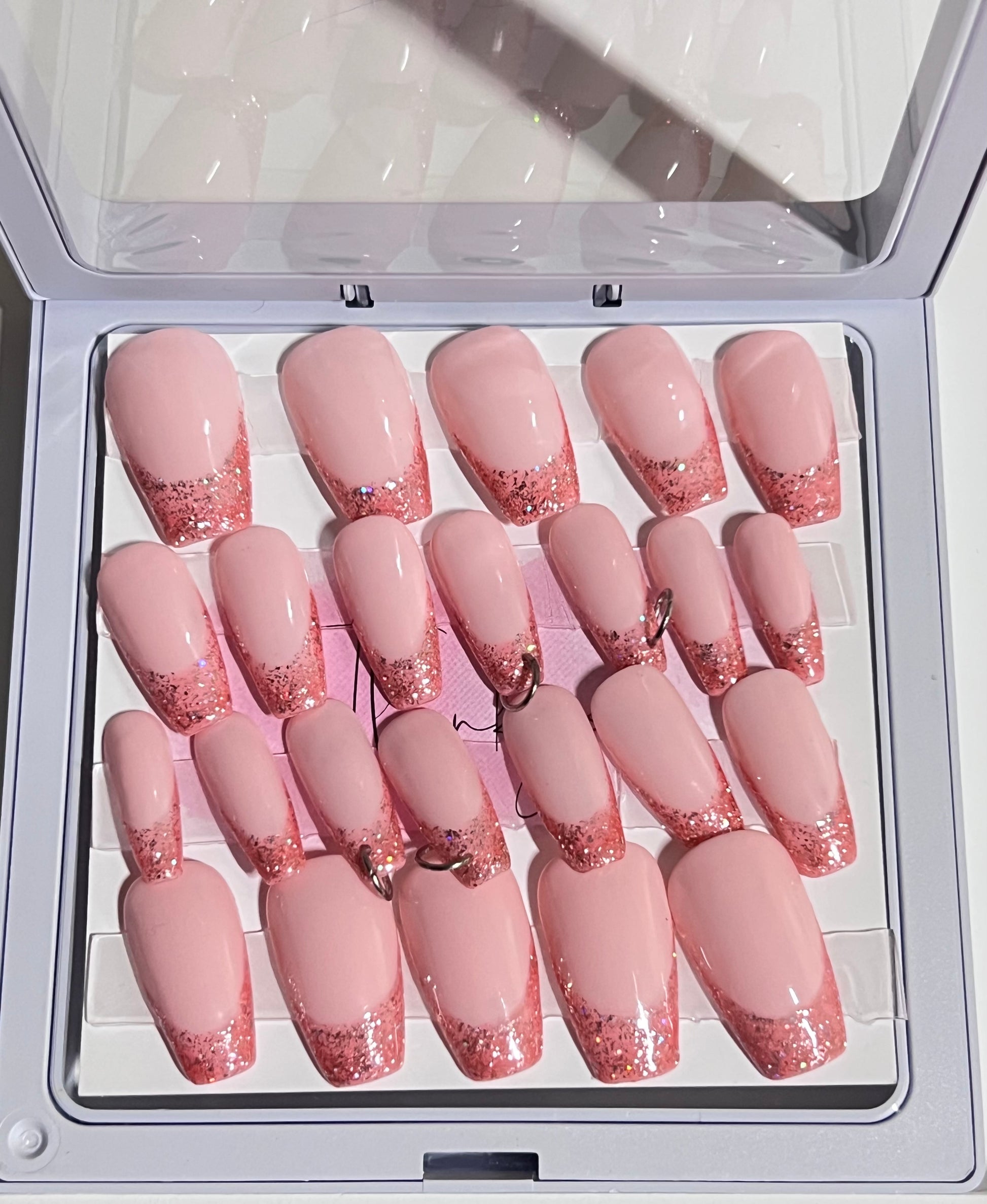 Set of 24 medium length coffin shaped nails with light pink/peach base and darker pink with glitter french tip. Included are 4 nails that are pierced with silver O rings and all are sealed with hard gel top coat.