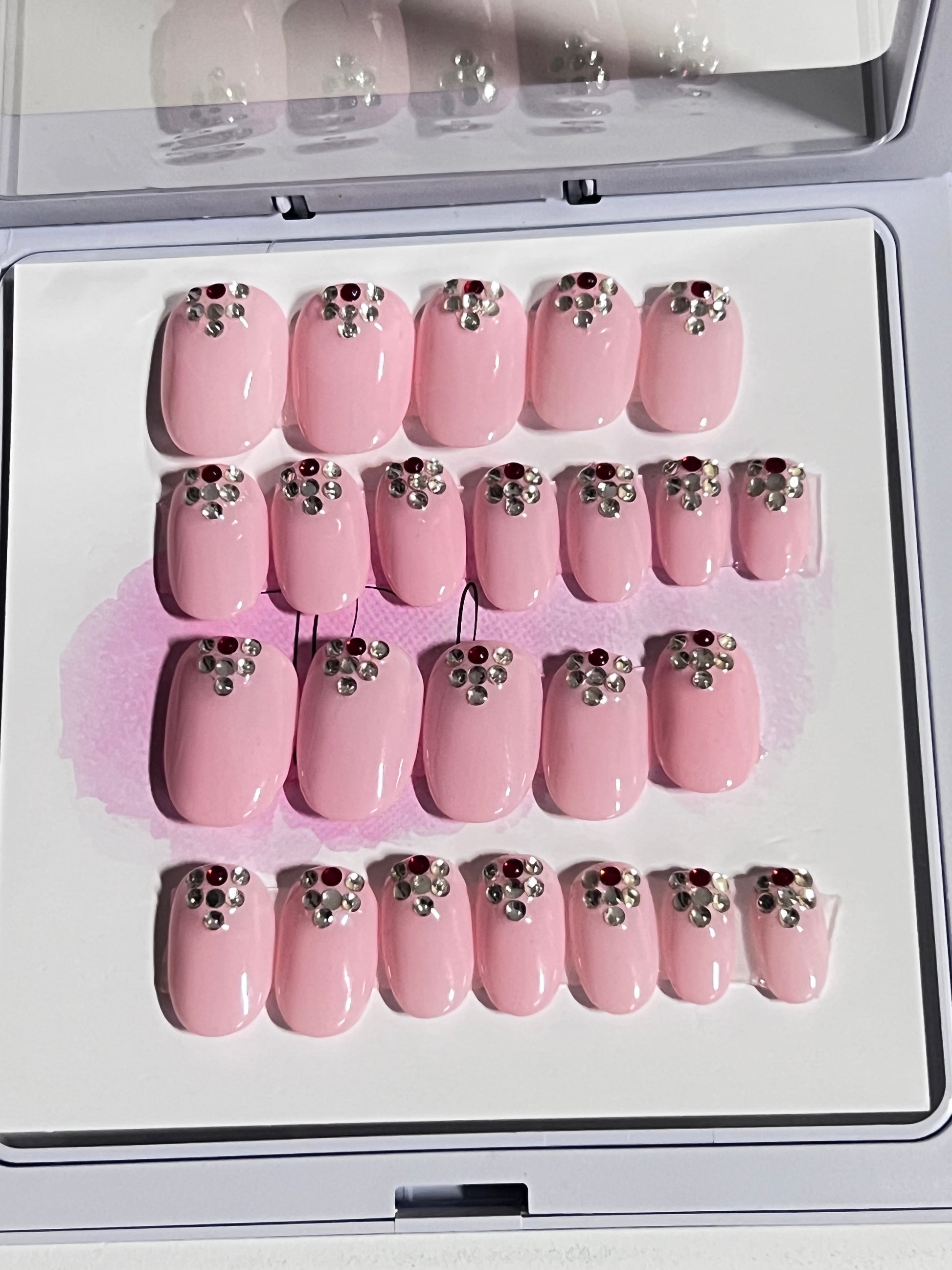 Set of 24 extra short oval nails with a light pink gel polish and stones at the cuticle sealed with a hard gel top coat. 