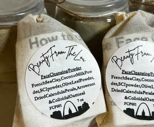 Two small beige drawstring pouches labeled 'Beauty From Lou' Face Cleansing Powder, shown in front of glass jars with clear lids. The round white labels list ingredients such as French sea clay, coconut milk powder, and SCi powder.