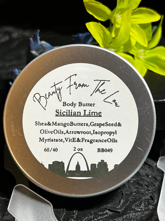 A round silver tin of Beauty From The Lou Body Butter in Sicilian Lime scent, featuring a white label with black text, set against a dark textured background with yellow flowers.