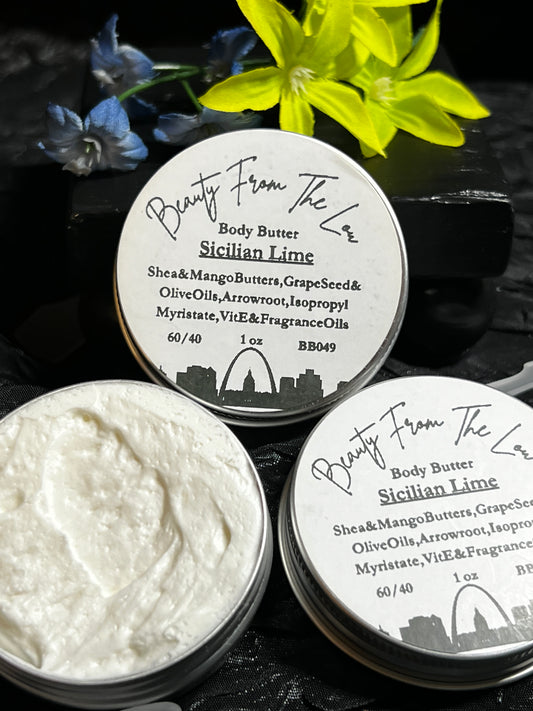 Three round metal tins of Sicilian Lime body butter are arranged on a dark textured surface with yellow flowers and blue blossoms. One tin is open, showing the thick white body butter cream inside, while the other two show the labeled lids.