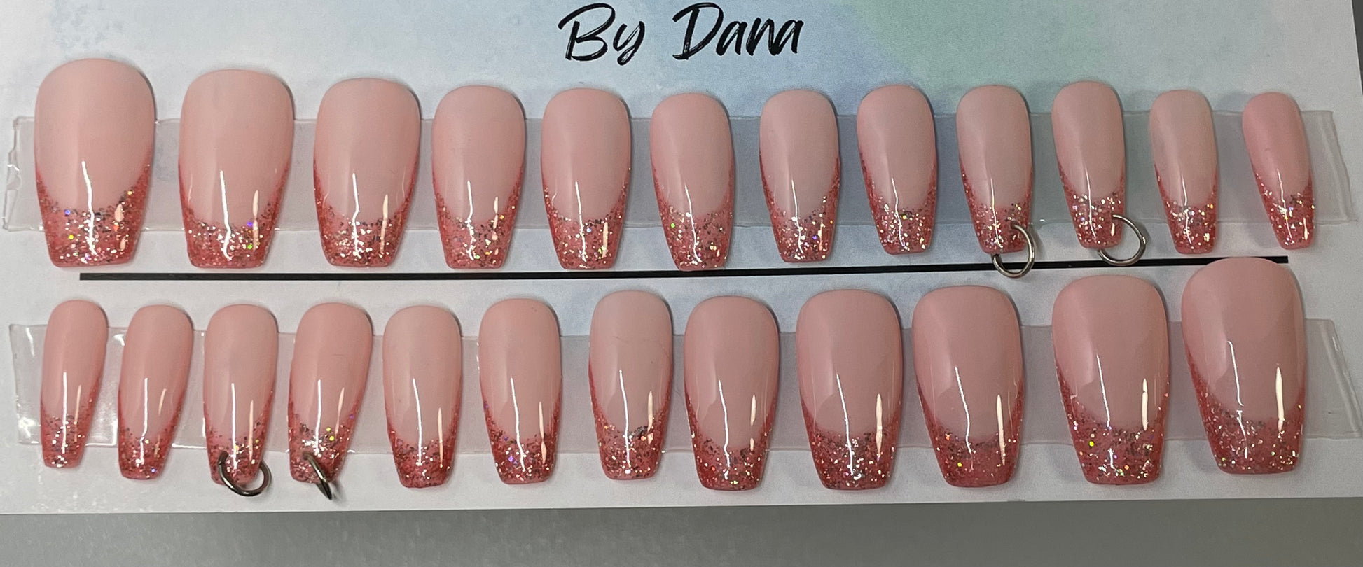 Professionally hand painted pink french. Soft pink nail bed and a darker pink tip w/ glitter. 4 nails have jump rings pierced into them.